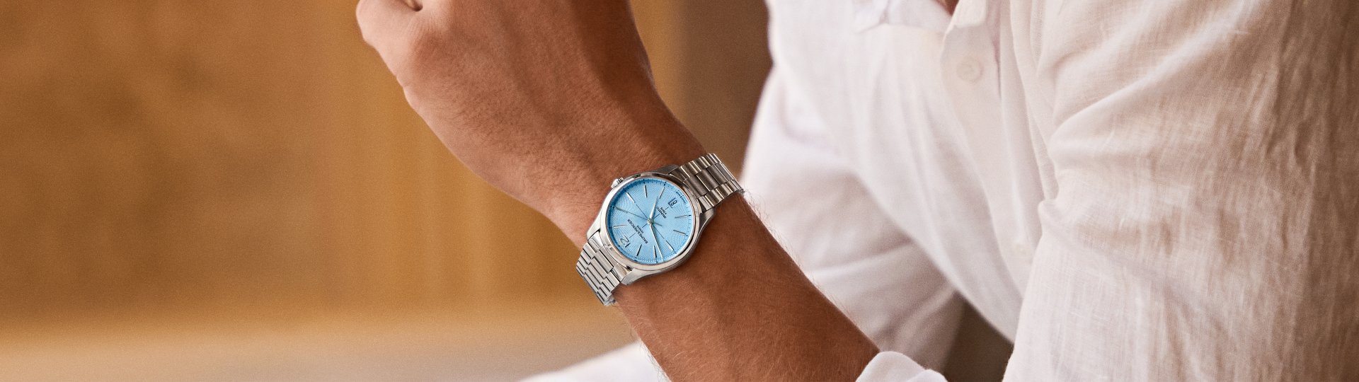 Mann im weißen Hemd trägt eine Clifton von Baume & Mercier mit Edelstahlarmband und eisblauem Zifferblatt.