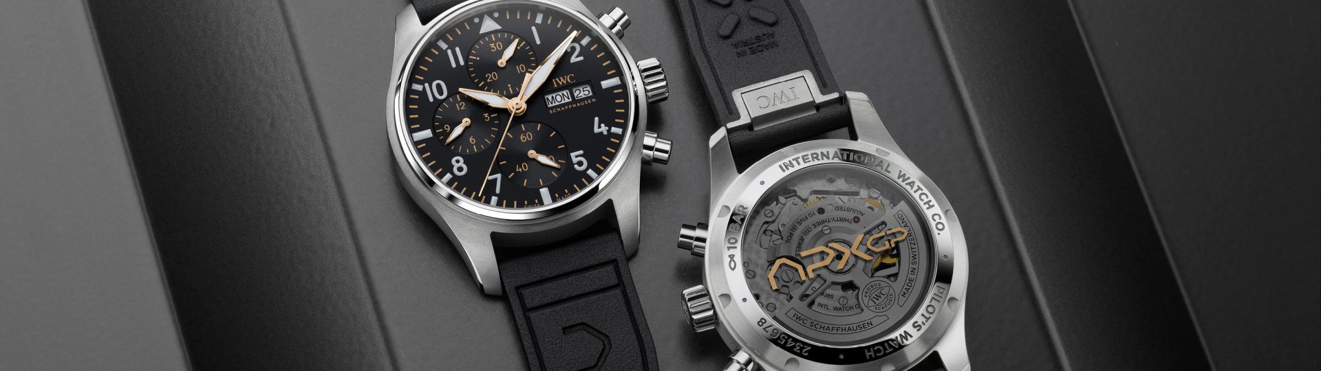 IWC Pilots Watch liegend von vorne und liegend von hinten auf grauem Hintergrund