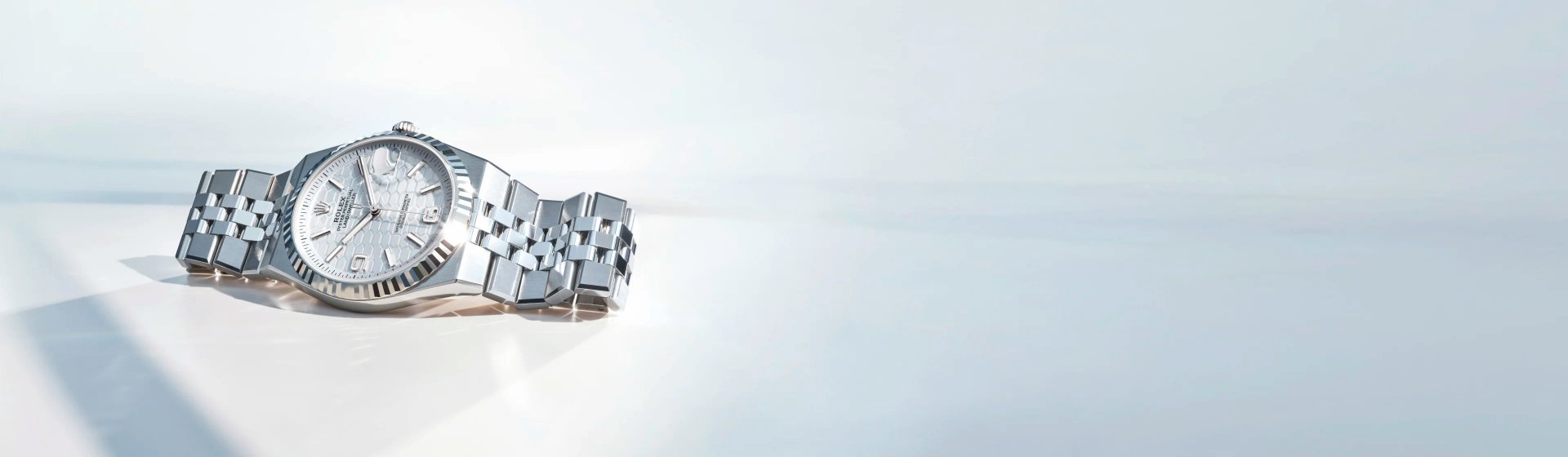 Rolex Land-Dweller aus Edelstahl mit geriffelter L&uuml;nette und silbernem Zifferblatt, elegant inszeniert auf hellem Hintergrund im Querformat.