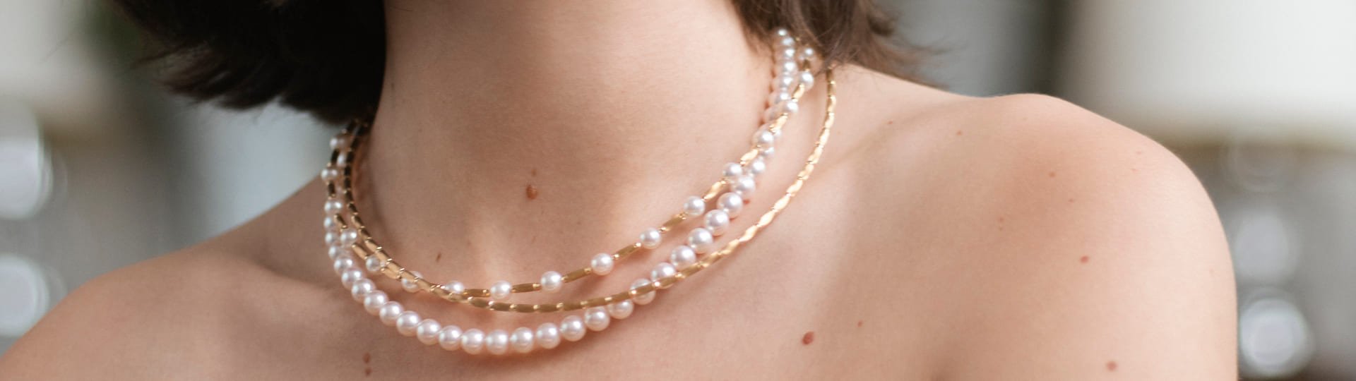 Nahaufnahme eines weiblichen Halses mit mehreren eleganten Halsketten aus weißen Perlen und goldenen Gliedern von Yana Nesper, die sich kunstvoll um den Hals schmiegen.