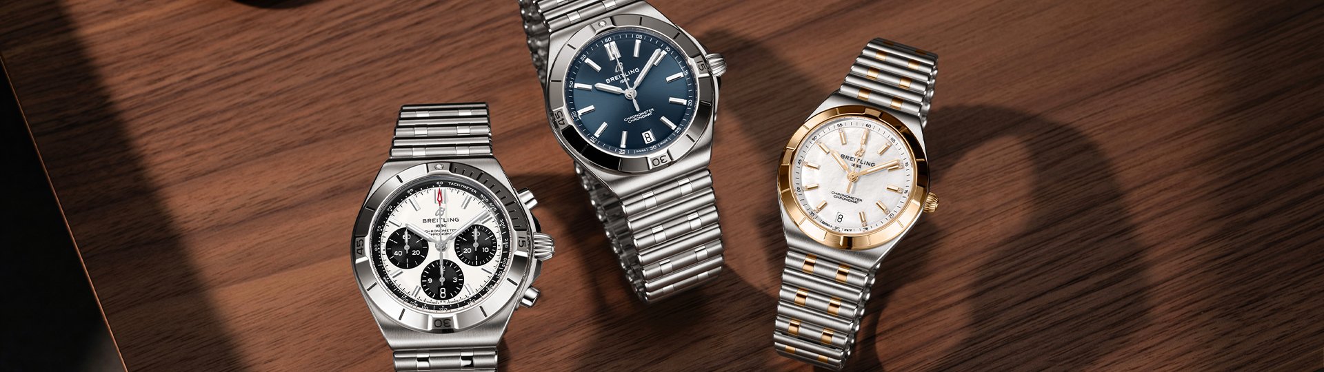 Breitling Chronomat Kollektion mit Chronomat B01 42 Chronograph, Automatic 40 mit blauem Zifferblatt und Automatic 36 in Bicolor auf edler Holzoberfl&auml;che.