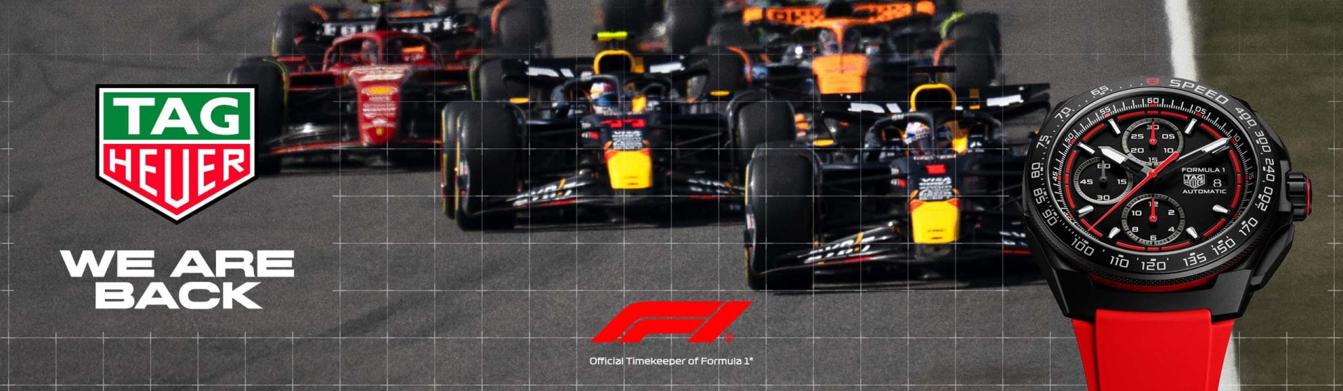 Tag Heuer Formula 1 Uhr mit schwarzem Gehaeuse und rotem Kautschukband vor Formula 1 Rennautos und links im Bild Tag Heuer Logo mit We are back Schriftzug