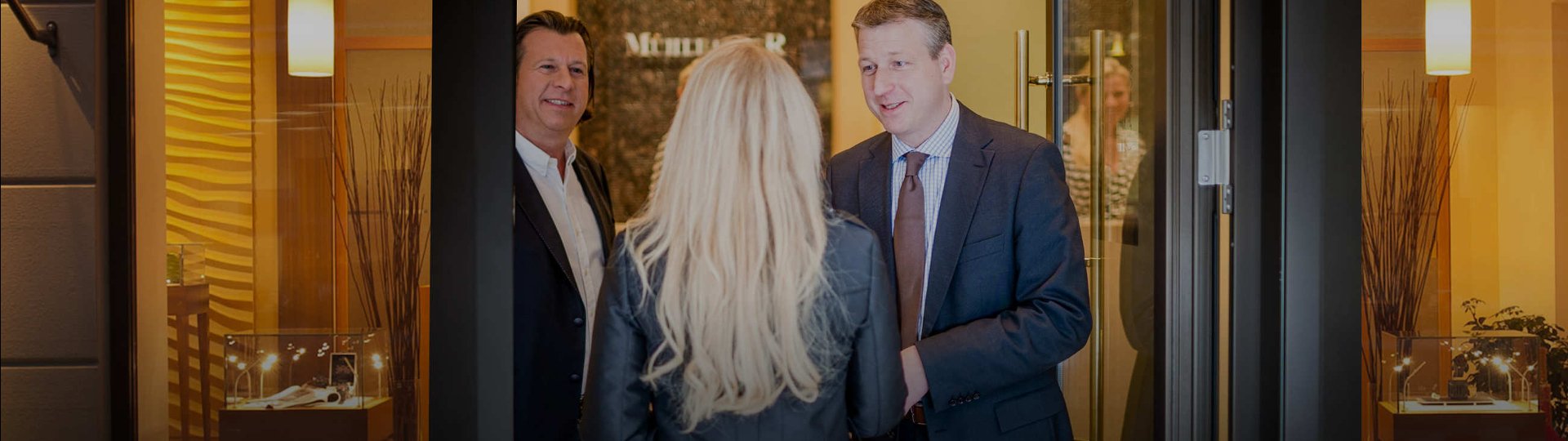 Die Geschaeftsfuehrer Andreas und Markus Muehlbacher begruessen an der Eingangstuer zum Juweliergeschaeft eine neue Mitarbeiterin