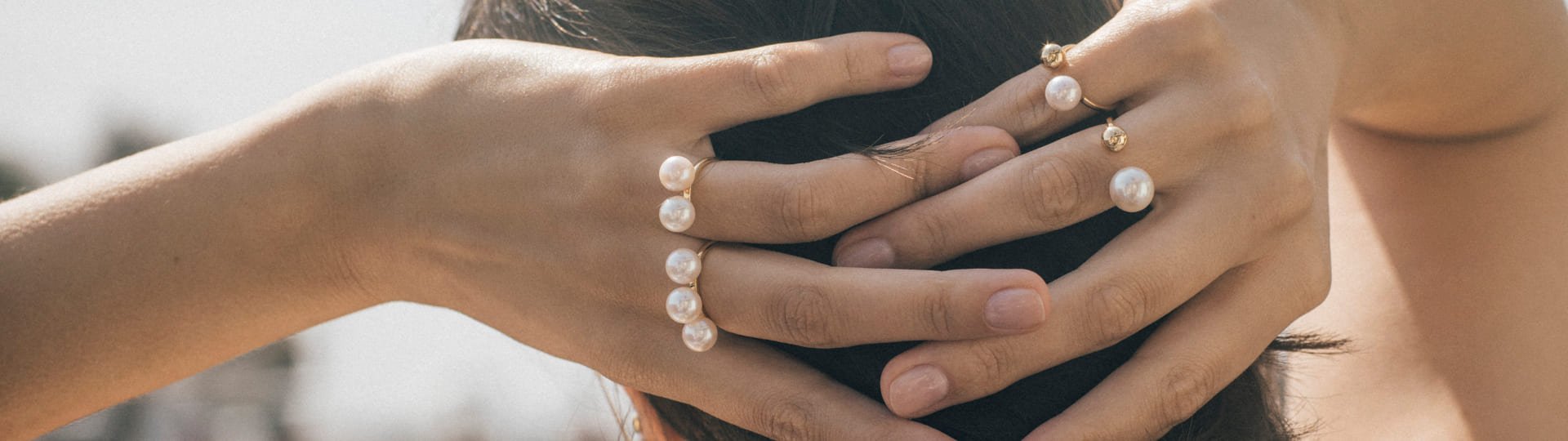 Luxuriöse Perlenringe von Yana Nesper an Frauenhänden, eleganter Goldschmuck mit weißen Süßwasserperlen, stilvolle Nahaufnahme vor hellem Hintergrund.