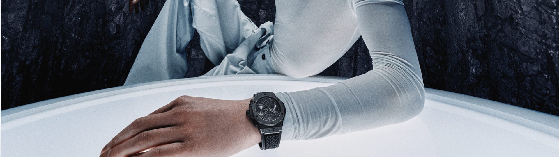 Junger Mann in futuristischem Setting mit heller Kleidung präsentiert eine Hublot Uhr mit schwarzem Gehäuse und Armband.