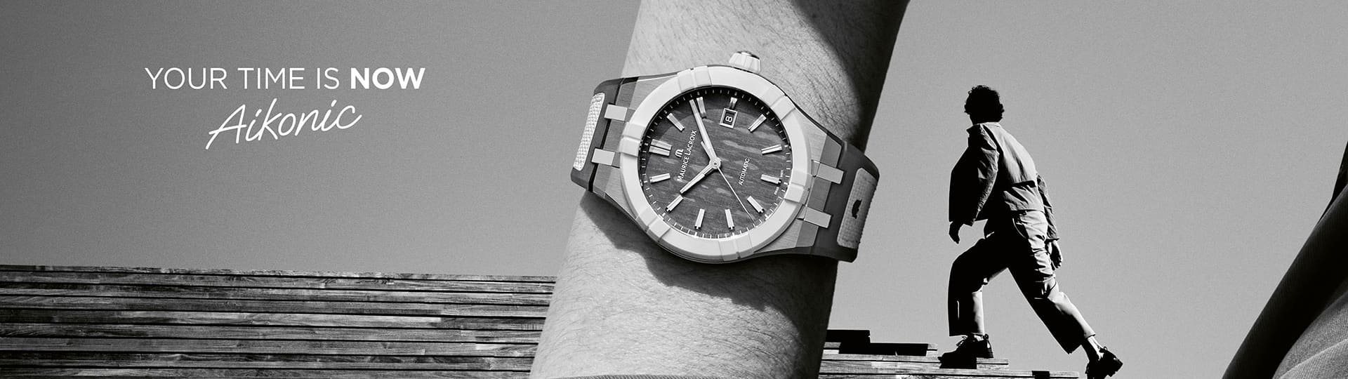 Schwarz-weiß-Werbemotiv mit Maurice Lacroix Aikonic Automatikuhr am Handgelenk, im Hintergrund ein Mann auf Holztreppe, Text: „Your Time is Now – Aikonic“.