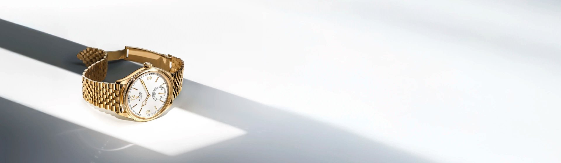 Rolex 1908 in Gelbgold mit Jubile-Armband und weißem Zifferblatt, stilvoll im Querformat fotografiert mit elegantem Lichteinfall für edle Produktpräsentation.