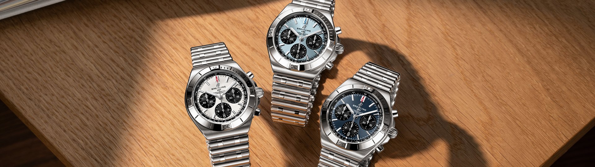 Drei Breitling Chronomat B01 42 Chronographen mit wei&szlig;en, eisblauen und dunkelblauen Zifferbl&auml;ttern auf heller Holzoberfl&auml;che.