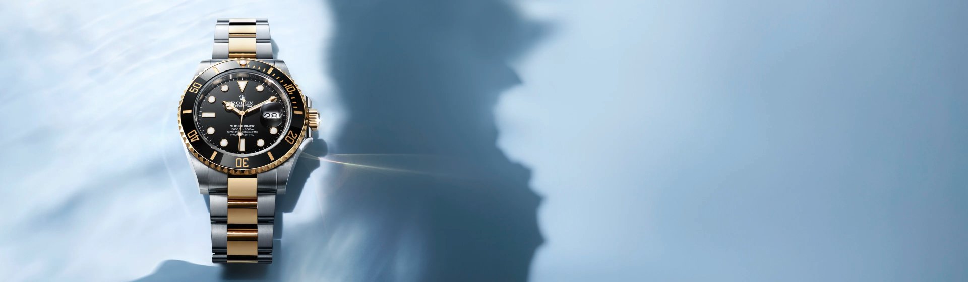 Rolex Submariner Date Rolesor Stahl-Gold mit schwarzer L&uuml;nette vor blauem Meereshintergrund mit Wasserreflexionen