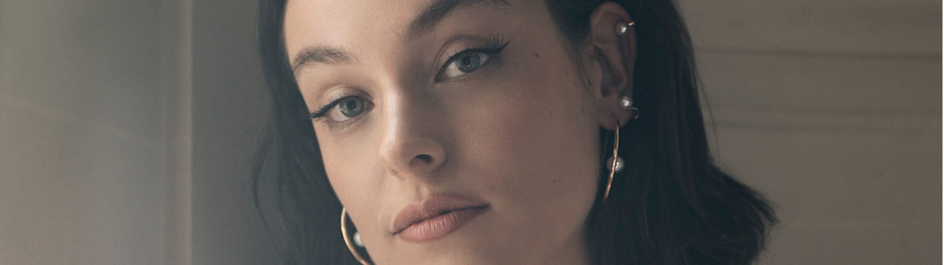 Nahaufnahme einer jungen Frau mit kurzen, dunklen Haaren und elegantem Ohrschmuck von Yana Nesper – goldene Creolen und mehrere Perlen-Ohrringe zieren ihr Ohr.