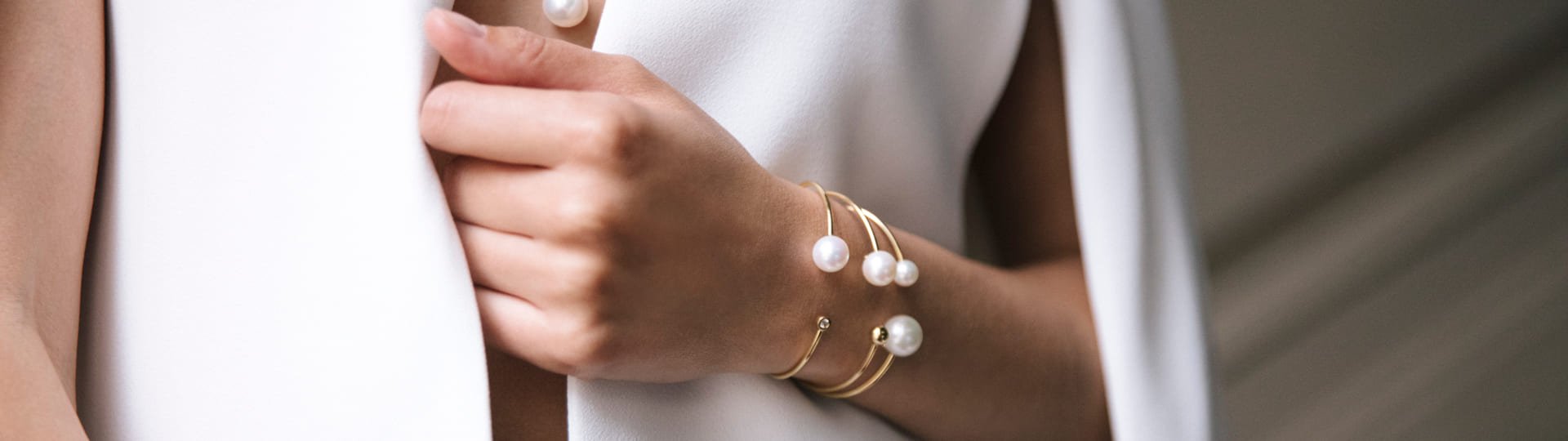 Nahaufnahme einer Hand mit elegantem Armschmuck von Yana Nesper: zarte goldene Armreifen mit weißen Perlen, minimalistischer und luxuriöser Look.