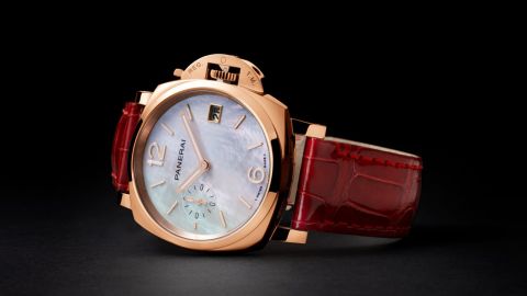 Panerai Luminor Due Uhr mit Goldtech Gehaeuse, weissem Perlmuttzifferblatt und rotem Lederarmband seitlich auf dunklem Untergrund liegend Panerai Luminor Due Uhr mit Goldtech Gehaeuse, weissem Perlmuttzifferblatt und rotem Lederarmband seitlich auf dunklem Untergrund liegend