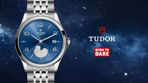 TUDOR 1926 Luna Armbanduhr mit Edelstahlarmband, blauem Zifferblatt mit Mondphase bei 6 Uhr, rechts daneben das rote TUDOR Logo und der Schriftzug „Born to Dare“ vor einem Nachthimmel.