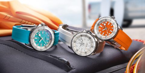 Drei Breitling Superocean Uhren mit Stahlgehaeusen, Zifferblaetter in tuerkis, weiss und orange und farbig identischen Kautschukarmbaender nebeneinander auf Lifestylehintergrund liegend