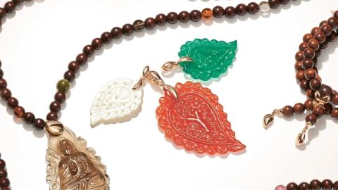 Drei India Anhaenger aus Perlmutt, gruenem und rotbraunem Onyx umgeben von Halsketten aus braunen Holzkugeln mit India Anhaenger aus grauem Chalcedon auf hellem Hintergrund liegend Drei India Anhaenger aus Perlmutt, gruenem und rotbraunem Onyx umgeben von Halsketten aus braunen Holzkugeln mit India Anhaenger aus grauem Chalcedon auf hellem Hintergrund liegend