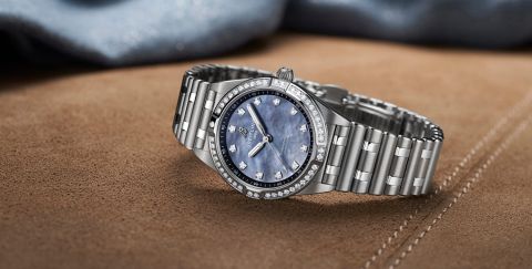 Breitling Chronomat Damenuhr in Stahl mit Diamanluenette, blauem Perlmutzifferblatt und Rouleauxarmband seitlich auf braunem Wildlederbezug liegend Breitling Chronomat Damenuhr in Stahl mit Diamanluenette, blauem Perlmutzifferblatt und Rouleauxarmband seitlich auf braunem Wildlederbezug liegend