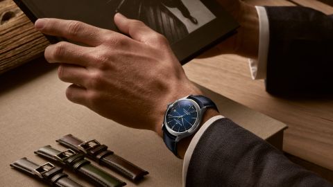 Mann im Anzug sitzt an einem Tisch und traegt eine Clifton Baumatic Uhr in Stahl mit blauem Zifferblatt und Lederarmband am Handgelenk Mann im Anzug sitzt an einem Tisch und traegt eine Clifton Baumatic Uhr in Stahl mit blauem Zifferblatt und Lederarmband am Handgelenk