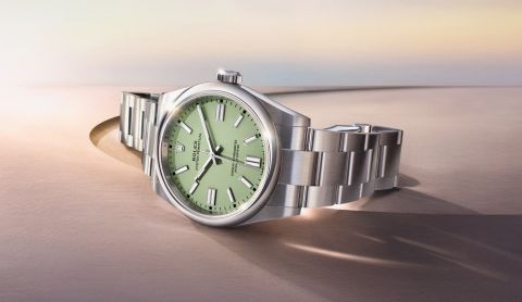 Rolex Oyster Perpetual in Stahl mit gruenem Zifferblatt seitlich auf braunem Untergrund liegend
