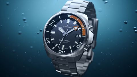 Junghans Aquaris Diver Taucheruhr aus Edelstahl mit dunkelgrauem Zifferblatt und Datumsanzeige vor blauem Unterwasser-Hintergrund.
