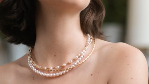 Nahaufnahme eines weiblichen Halses mit mehreren eleganten Halsketten aus weißen Perlen und goldenen Gliedern von Yana Nesper, die sich kunstvoll um den Hals schmiegen.