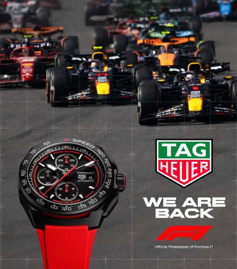 Tag Heuer Formula 1 Uhr mit schwarzem Gehaeuse und rotem Kautschukband vor Formula 1 Rennautos und Tag Heuer Logo mit We are back Schriftzug
