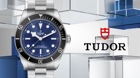 Links Tudor Black Bay 68 Uhr in Stahl mit schwarzer Luenette und blauem Zifferblatt, rechts daneben TUDOR Logo vor blau-grauem Lifestylehintergrund