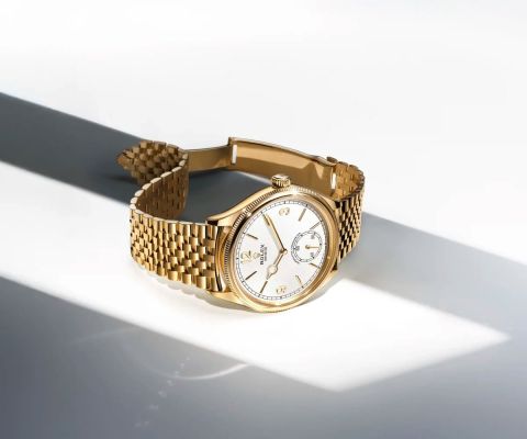 Rolex 1908 Armbanduhr aus 18 Karat Gelbgold mit weißem Zifferblatt, Goldzeigern und Jubile-Armband, luxuriös präsentiert im Spiel von Licht und Schatten.