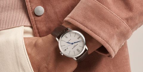 Baume Mercier Classima Uhr in Stahl mit weissem Zifferblatt und braunem Lederarmband an einem Herrenhandgelenk getragen Baume Mercier Classima Uhr in Stahl mit weissem Zifferblatt und braunem Lederarmband an einem Herrenhandgelenk getragen