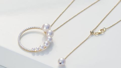 Goldene Kette von Yana Nesper mit weißen Perlen und rundem Anhänger auf weißer Fläche. Goldene Kette von Yana Nesper mit weißen Perlen und rundem Anhänger auf weißer Fläche.