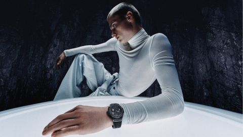 Junger Mann in futuristischem Setting mit heller Kleidung präsentiert eine Hublot Uhr mit schwarzem Gehäuse und Armband.