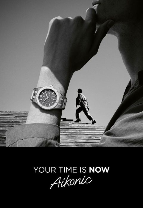 Stilvolle Maurice Lacroix Aikonic Uhr am Handgelenk eines Mannes in Denkerpose, Person steigt Treppe hoch, Schwarz-Weiß-Look mit Slogan "Your time is now Aikonic".