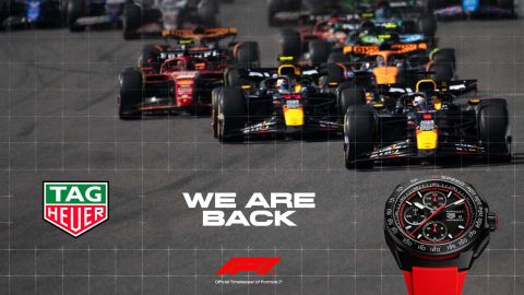 Tag Heuer Formula 1 Uhr mit schwarzem Gehaeuse und rotem Kautschukband vor Formula 1 Rennautos und links im Bild Tag Heuer Logo mit We are back Schriftzug Tag Heuer Formula 1 Uhr mit schwarzem Gehaeuse und rotem Kautschukband vor Formula 1 Rennautos und links im Bild Tag Heuer Logo mit We are back Schriftzug