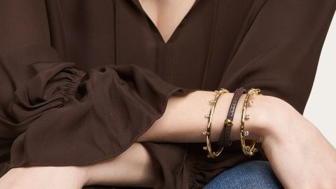 Weibliches Model mit 2 Gypsy Armreifen in Gelbgold mit Diamanten und braunem Lederband mit Signature Charm am Handgelenk getragen Weibliches Model mit 2 Gypsy Armreifen in Gelbgold mit Diamanten und braunem Lederband mit Signature Charm am Handgelenk getragen