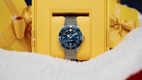 Nahaufnahme einer blauen Breitling Superocean Uhr in einer gelben Geschenkbox, eingerahmt von weißem Winterfell und goldenen Geschenkpaketen im Hintergrund.