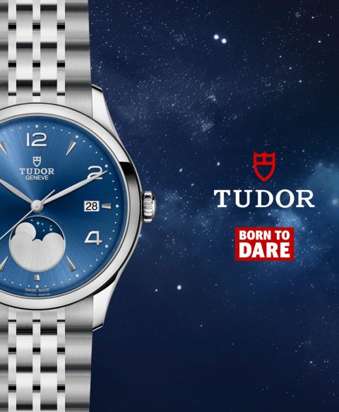 TUDOR 1926 Luna Armbanduhr mit Edelstahlarmband, blauem Zifferblatt mit Mondphase bei 6 Uhr, rechts daneben das rote TUDOR Logo und der Schriftzug „Born to Dare“ vor einem Nachthimmel.