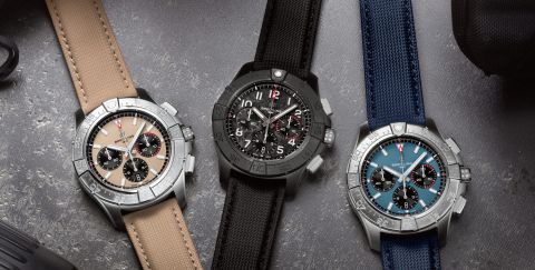 Drei Breitling Avenger Chronographen auf grauem Hintergrund, links in Stahl, beiges Zifferblatt, mittig schwarze Keramik, schwarzes Zifferblatt, rechts in Stahl, blaues Zifferblatt