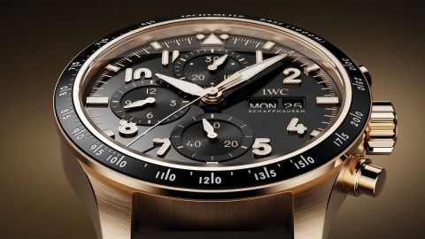 IWC Pilots Watch in Gold mit schwarzer Luenette und Zifferblatt vor braungold-schwarzem Hintergrund